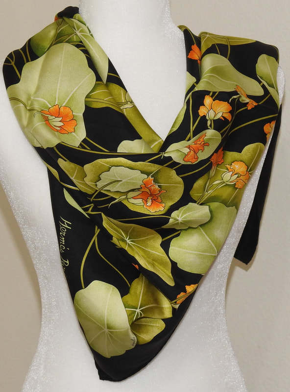 Picture of Les Capucines, a used Hermes 90cm silk scarf for sale. This black and green colorway is knotted in a simple triangle