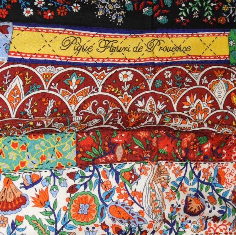 Close up picture of Pique Fleuri en Provence, a multi-color floral Hermes 140cm silk and cashmere scarf issued in 2012. Designed by Christine Henry, it features bright orange and yellow, brick red, several shades of blue, and several shades of green