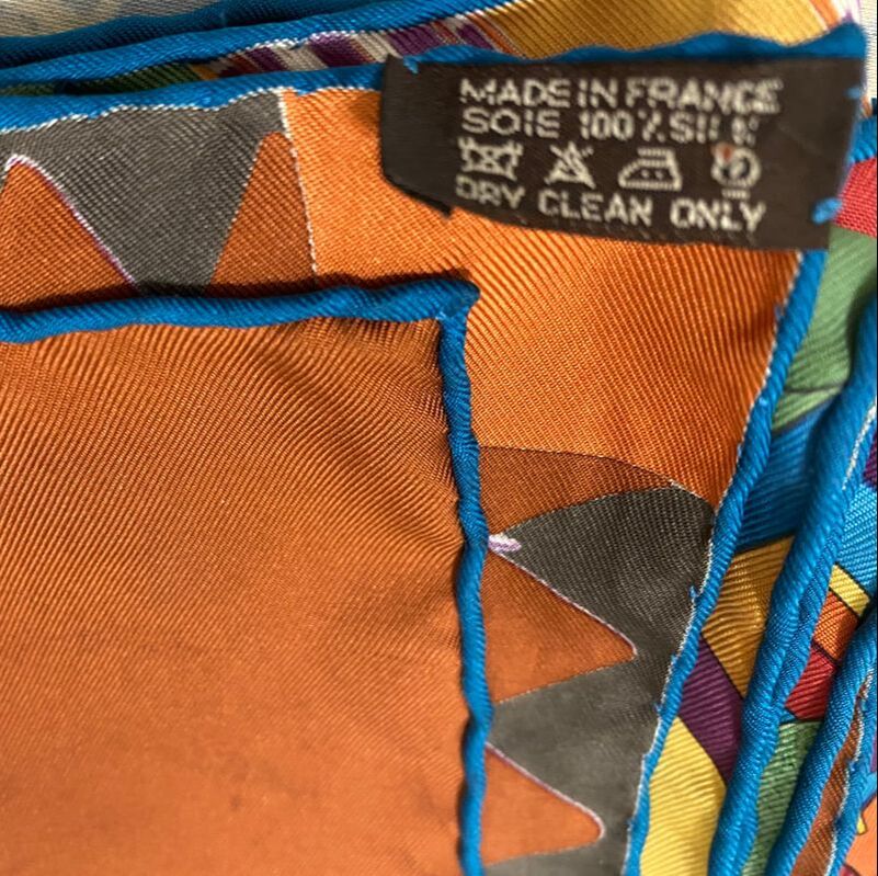 Closeup picture of caretag on Coupons Indiens, a used Hermes 90cm silk scarf for sale. This scarf is brown and blue and green and yellow and purple