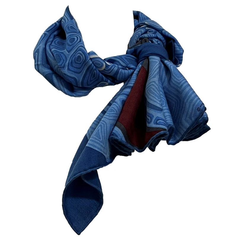 Picture of a knotted Hermes cashmere scarf, Aaaaargh. This 100cm men's scarf has a blue dinosaur against a blue background and an orange eye