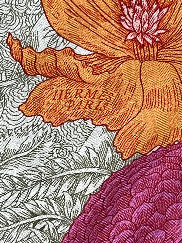 Close up picture of the Hermes brand appearing in a used Hermes 140cm cashmere scarf Retour a la Nature featuring orange and pink flowers and birds
