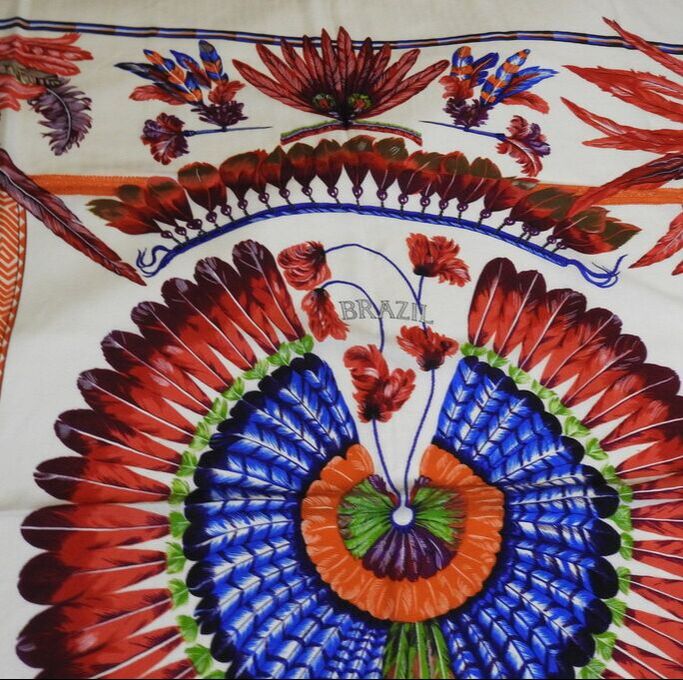 Close up picture of Brazil, a white Hermes 140cm silk and cashmere scarf issued in 2009. Designed by Toutsy, it features bright red and orange, blue and green feathers