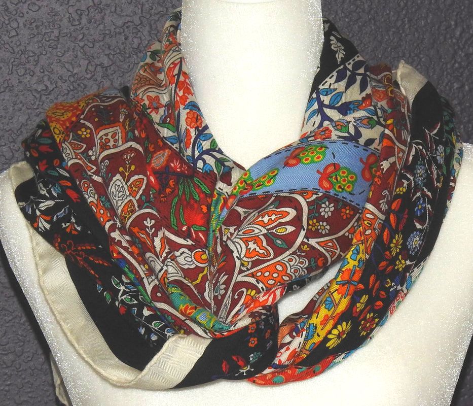 Picture of used Hermes 140cm silk and cashmere scarf for sale. Pique Fleuri en Provence by Christine Henry, knotted in an infinity knot. Black background, red, orange, blue, green and white flowers